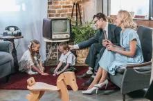glückliche Eltern sitzen auf dem Sofa und schauen sich kleine Kinder an, die zu Hause mit Dominosteinen spielen, Stil der 50er Jahre