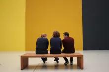 Drei Menschen auf einer Bank in einer Ausstellung